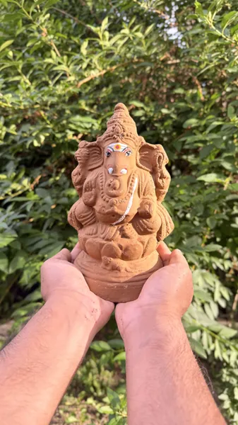 Close-up of a handmade natural clay Ganesha idol held outdoors