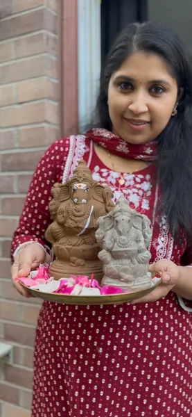 Two handmade natural clay Ganesha idols held on a brass plate with rose petals