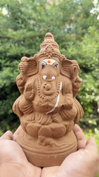 Hands holding a handmade plantable clay Ganesha idol in a garden