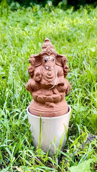Plantable clay Ganesha idol standing in a white planter pot on garden grass